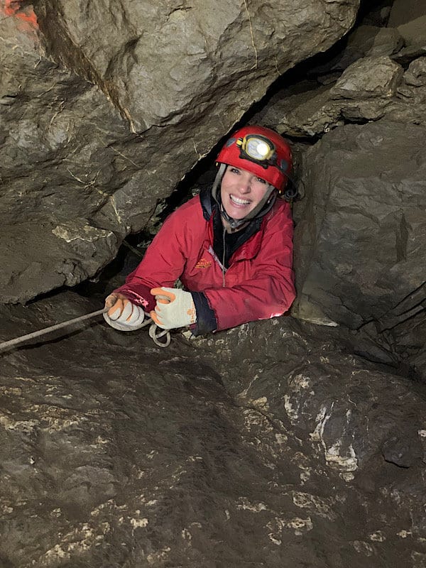 strahlend lächelnde Frau die sich durch eine Engstelle in der Hölloch-Höhle quetscht