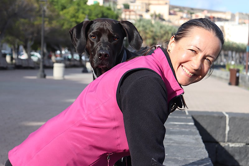 Petra steht an Hafenmauer und Hund Amor blickt über ihre Schulter direkt in deine Augen