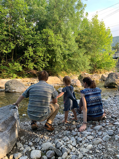 Familie mit kleinem Kind sitzt am Bach und beobachtet den Wasserlauf.
