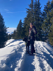 Petra steht mit Hund Amor auf dem Berggrat im Schnee.
