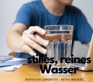 Man greift zum Wasserglas. Er sitzt am Tisch vor dem Laptop.
