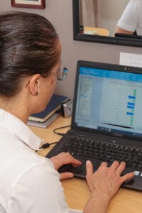 Petra sitzt vor dem Bildschirm und sieht die Auswertung der Vitaldatenmessung.