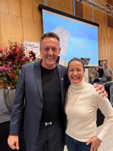 Joachim Heberlein ist mit Petra Büeler auf dem Bild. Im Hintergrund eine Leinwand, die Evelyn Binsack zeigt und ebenfalls 3 menshen im hintergrund, einer davon ist Joey Kelly von der "Kelly Family"