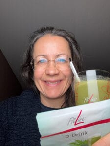 Petra hält ein grünes Getränk und wünscht prost.