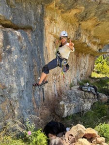 Petra sitzt im Klettergurt und das Seil hält sie. Sie lächelt in die Kamera und wirkt sehr glücklich