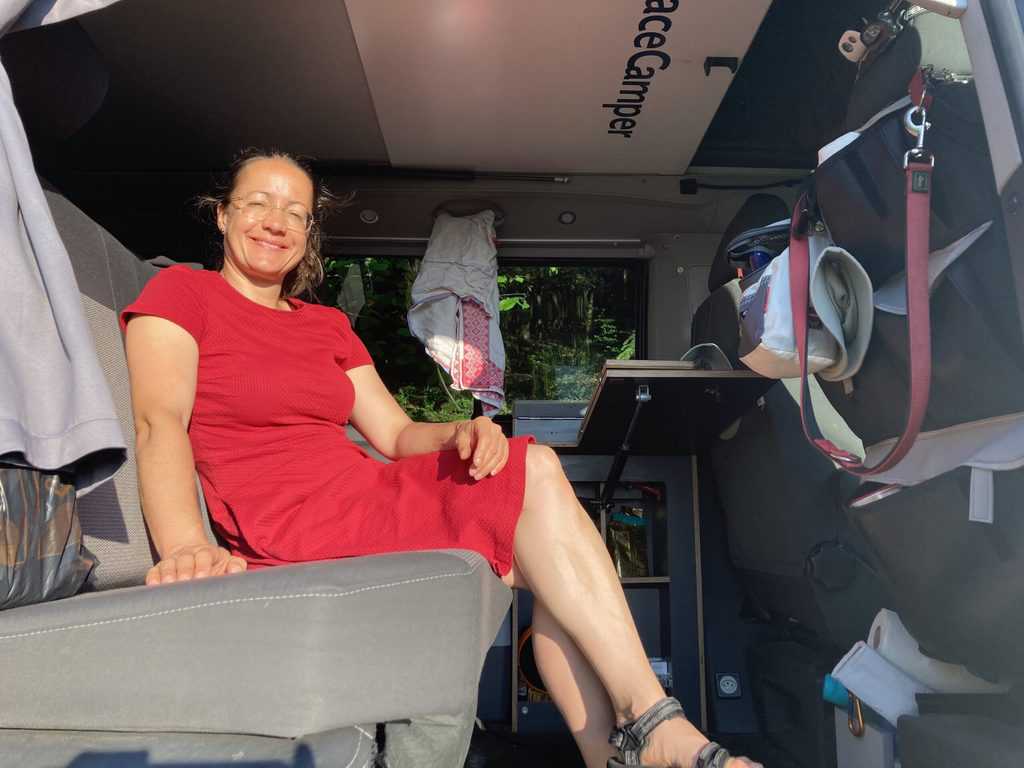 Petra sitzt sim roten Kleid auf der Rückbank im VW Bus