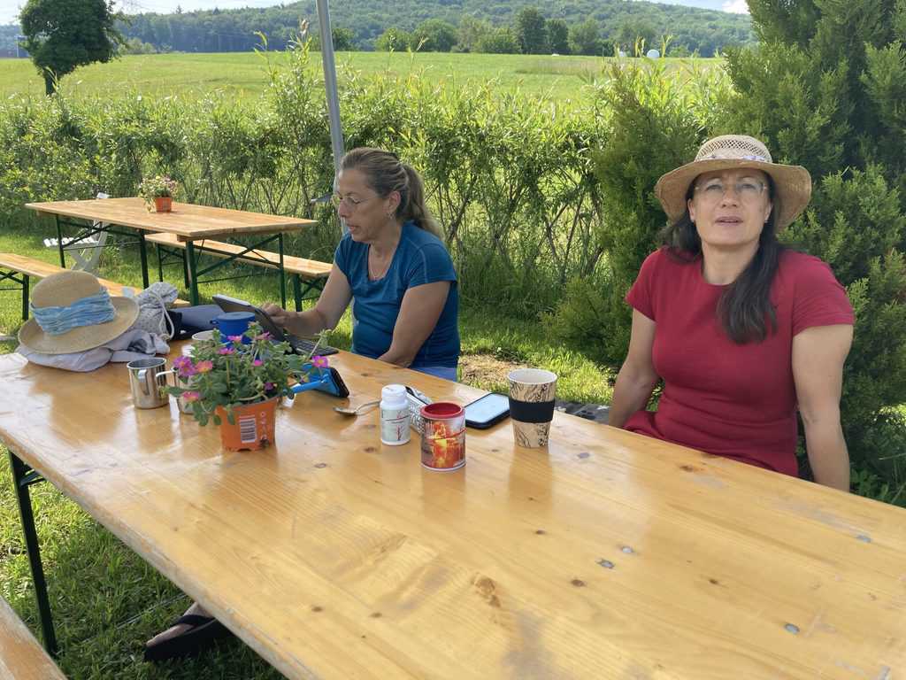 Zwei Frauen sitzen an einem Gartentisch und schauen zusammen auf einem iPad eine Schulung