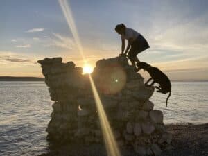 Hund und Frauchen auf Ruinenstück am Klettern während des Sonnenuntergangs