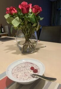 Frühstücksschale mit Joghurt, Leinsamen und Sonnenblumenkernen. Dekoriert mit 2 Himbeeren und im Hintergrund ein Strauss Rosen